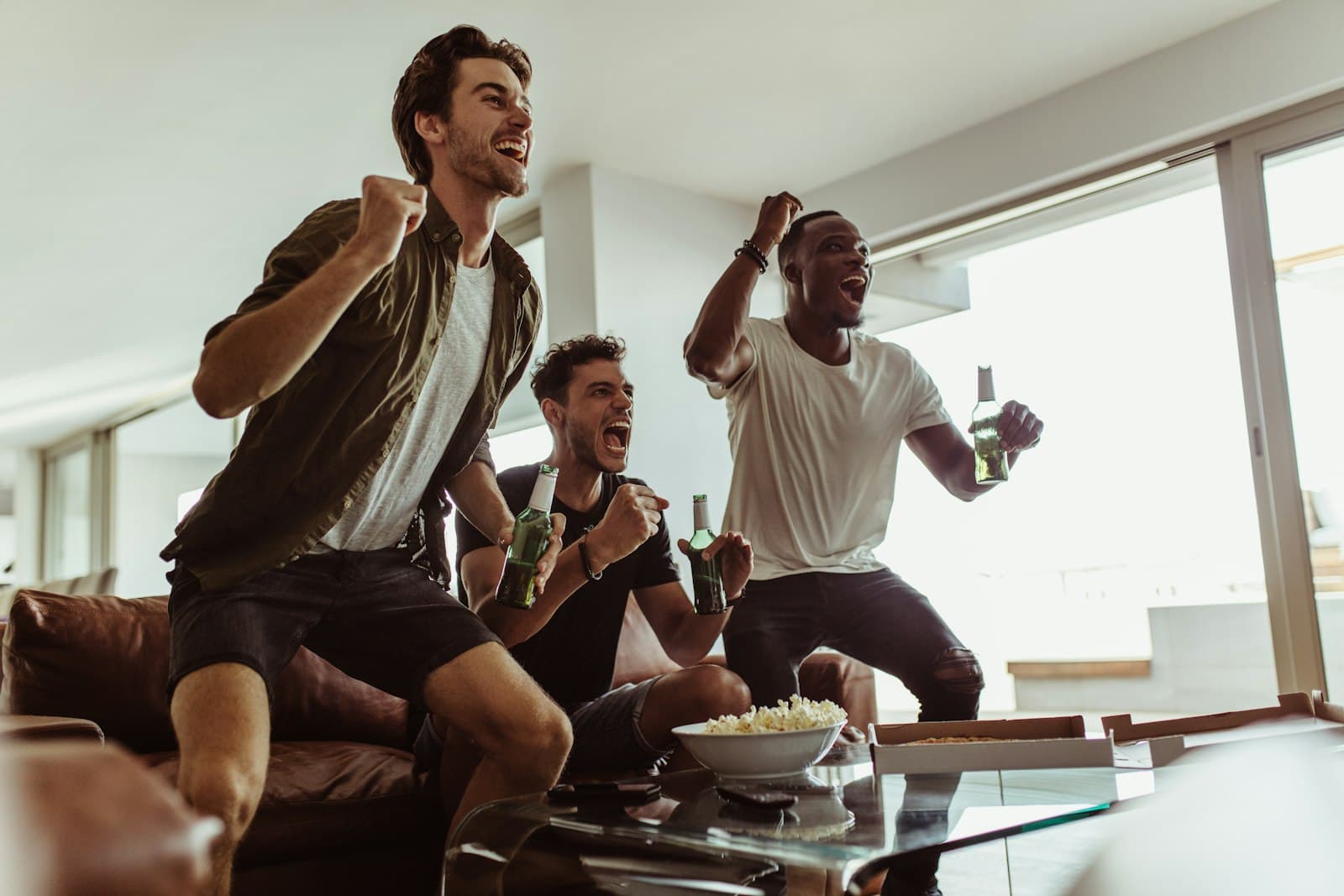 Three friends celebrating on a couch with drinks while watching a game