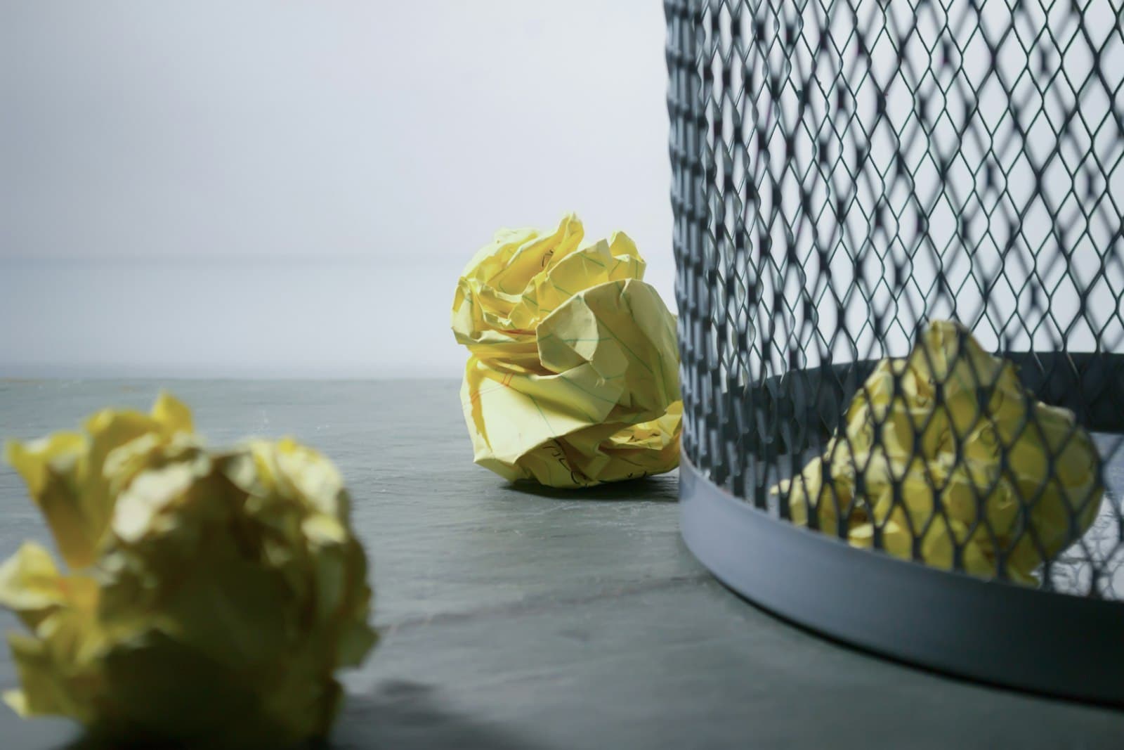 Crumpled yellow note pages scattered around a wire wastebasket