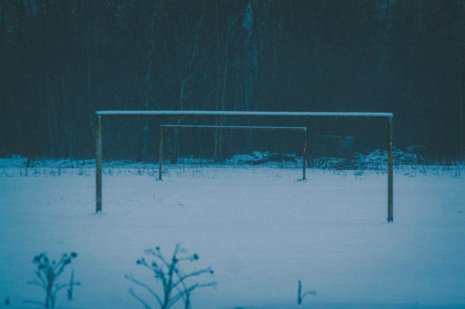 Snow-covered field with empty goalposts at winter dusk