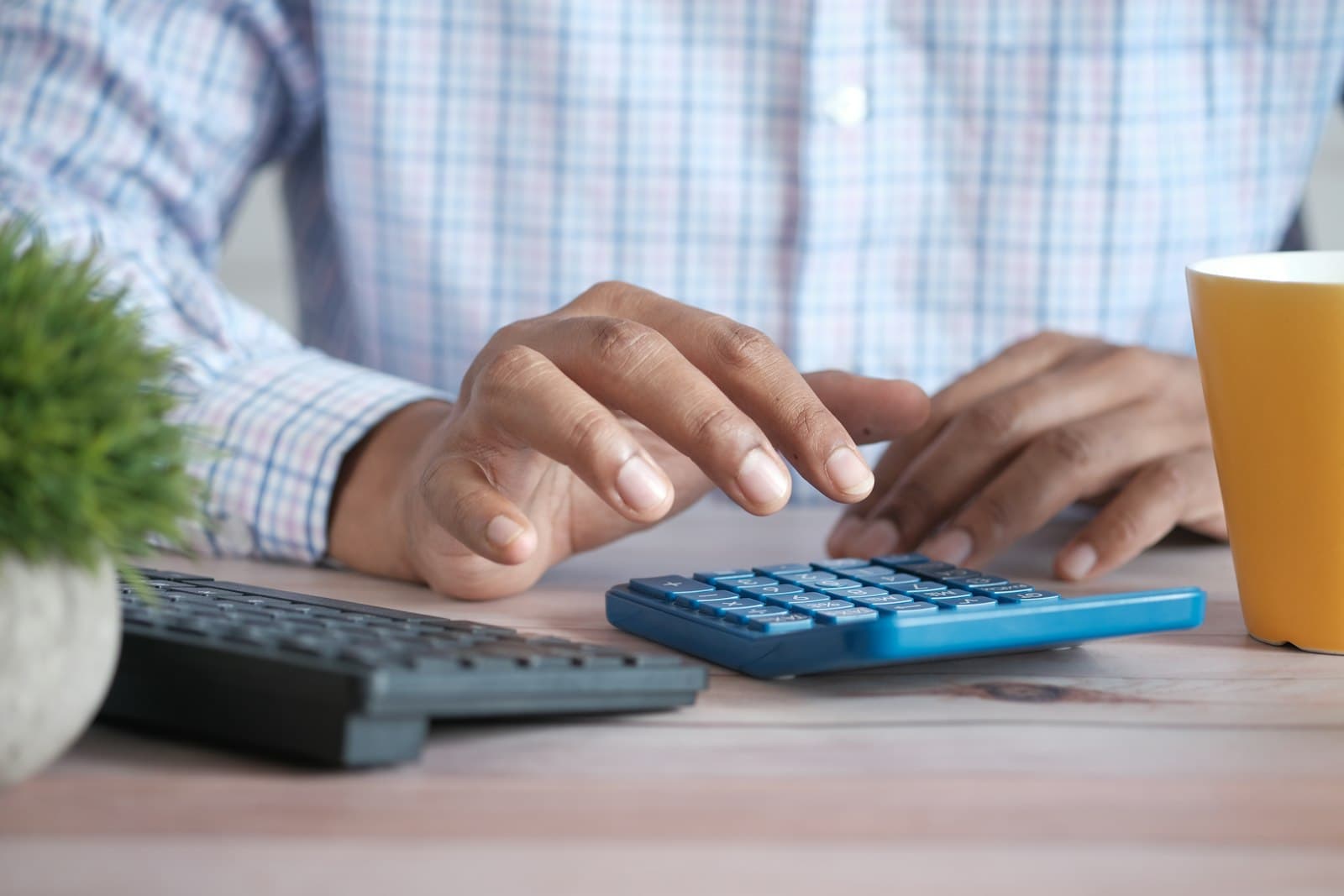 Hands using a calculator at a desk beside a coffee mug