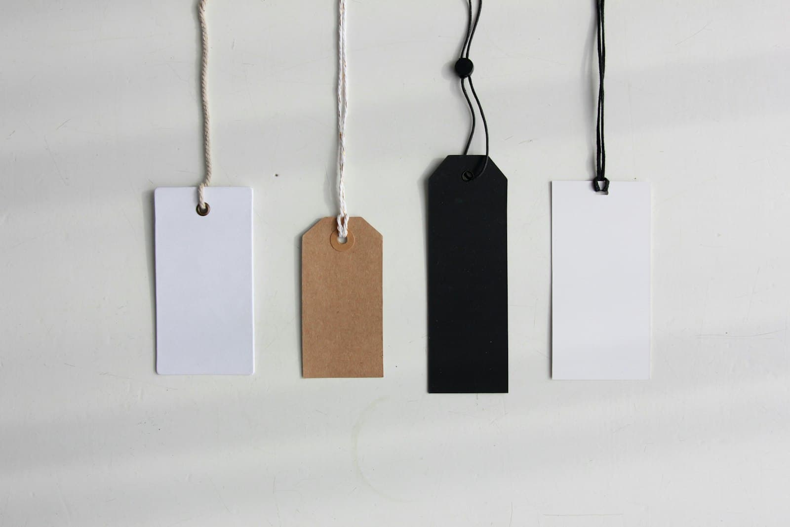 Four blank price tags hanging from strings against a white wall