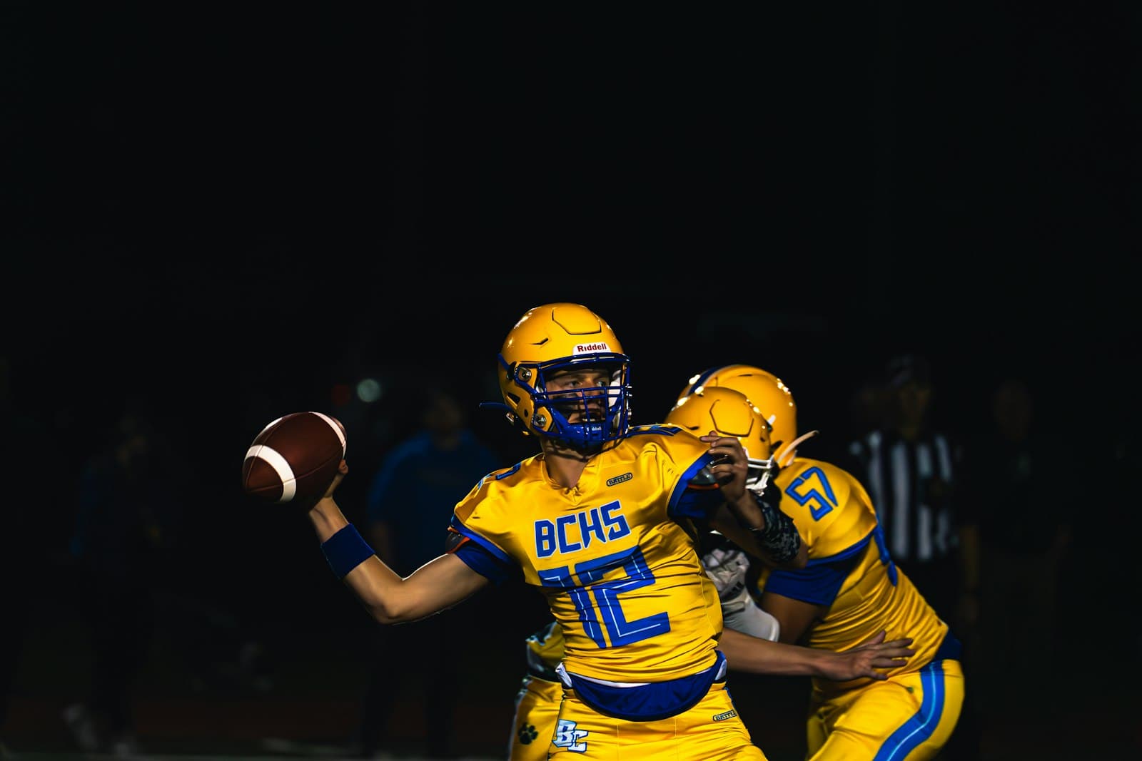 High school quarterback throwing a pass under stadium lights at night