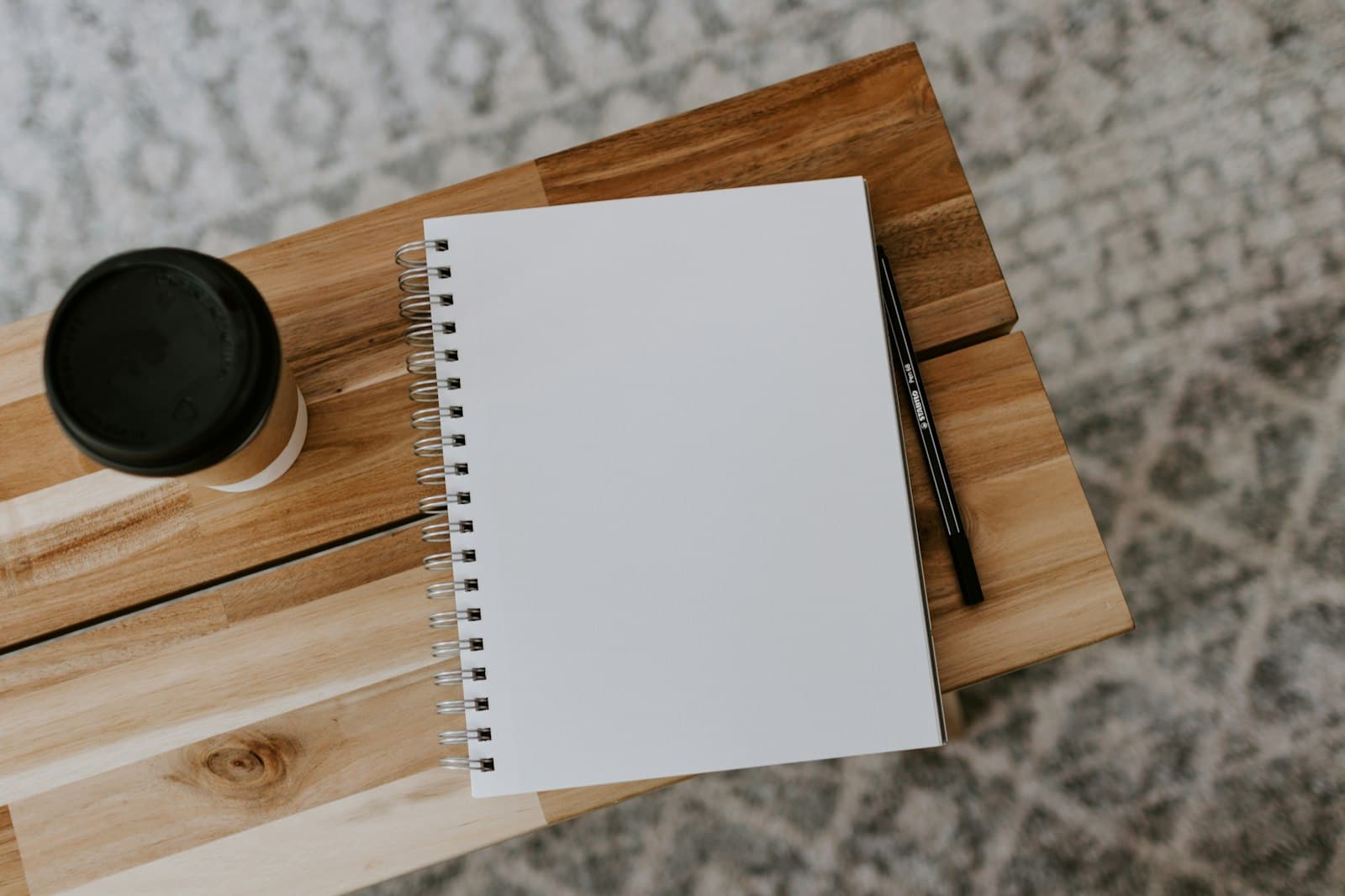 Blank spiral notebook with a pen and takeaway coffee on a wooden table