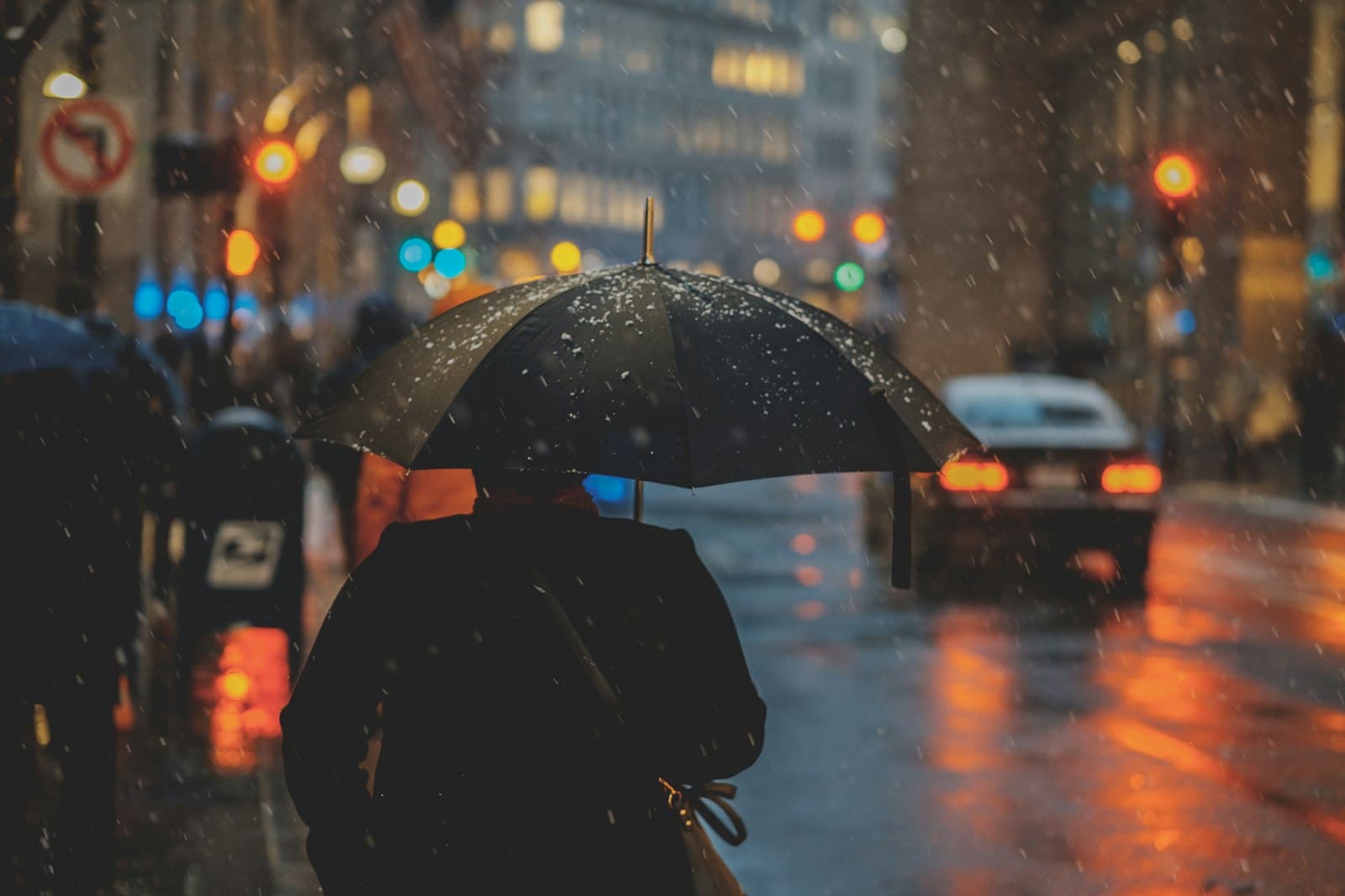 Person walking through city rain under a black umbrella