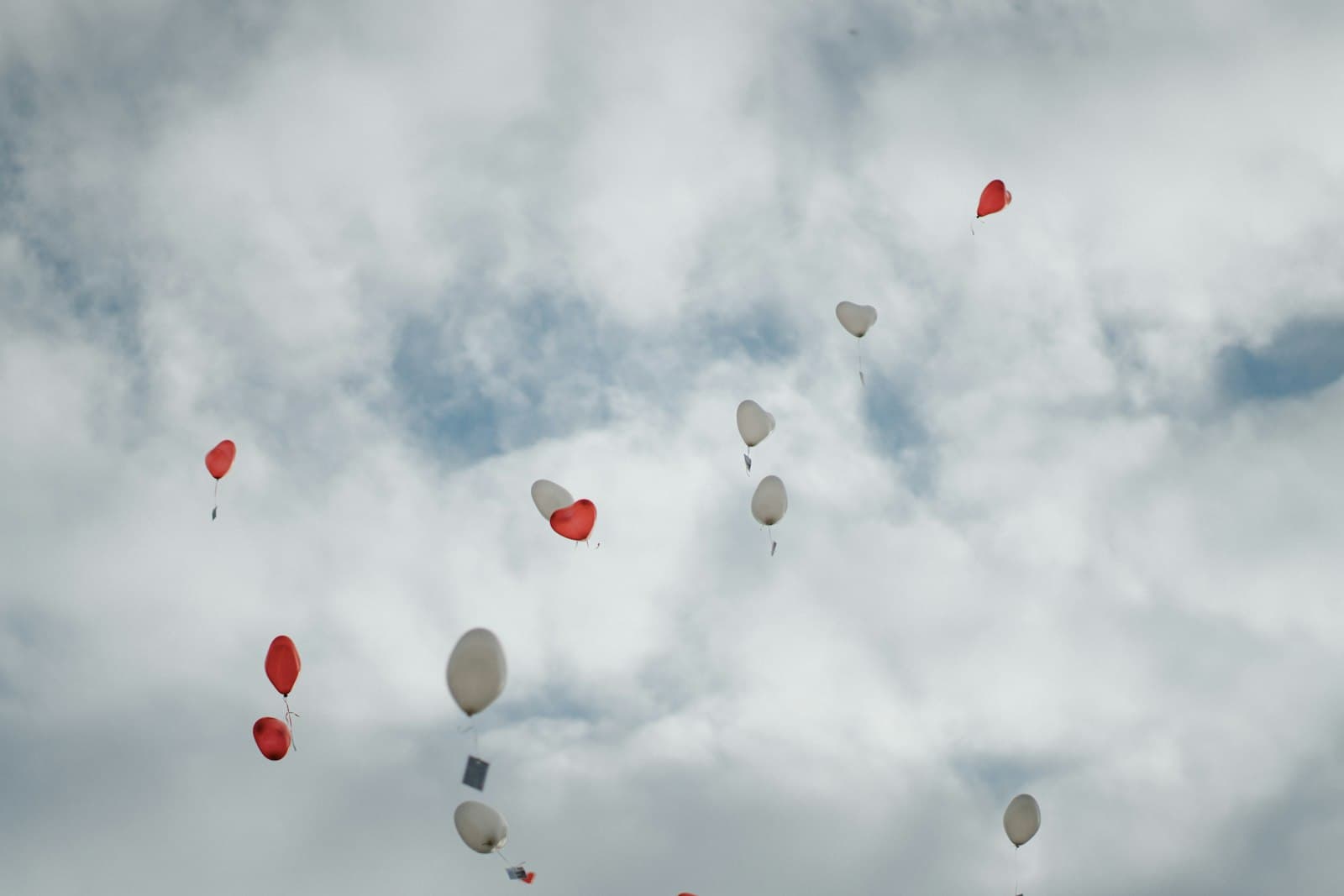 Red and white balloons floating up into a cloudy sky