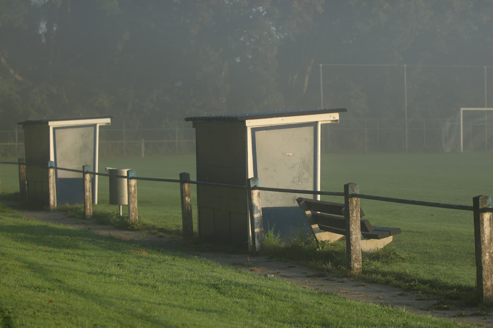 Empty benches and dugout shelters beside a foggy practice field