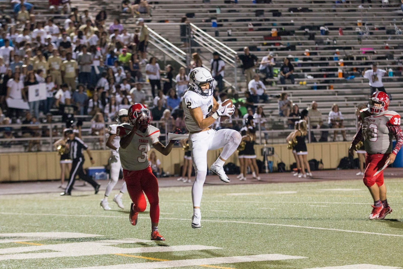 Receiver leaping to catch a football in front of the end zone stands